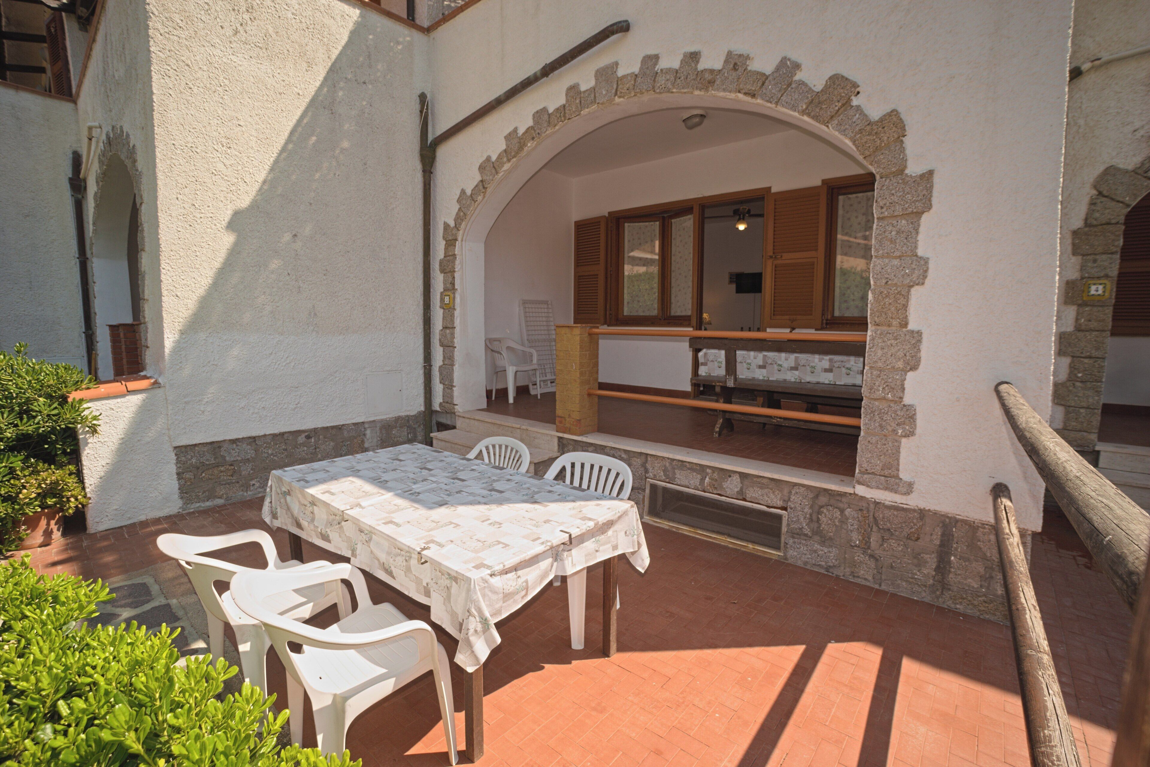Une terrasse extérieure avec une table et des chaises, une arche en pierre et une vue sur une pièce dotée d’une fenêtre et d’un banc.