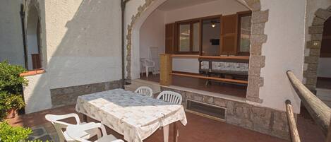 Une terrasse extérieure avec une table et des chaises, une arche en pierre et une vue sur une pièce dotée d’une fenêtre et d’un banc.