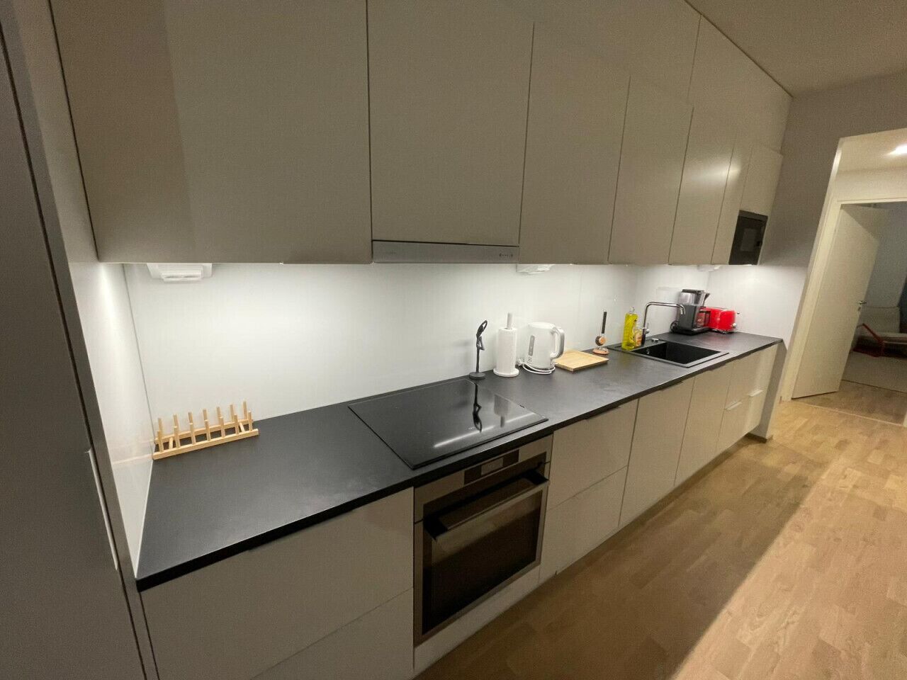 Una cocina moderna con encimera negra, electrodomésticos de acero inoxidable y horno empotrado.