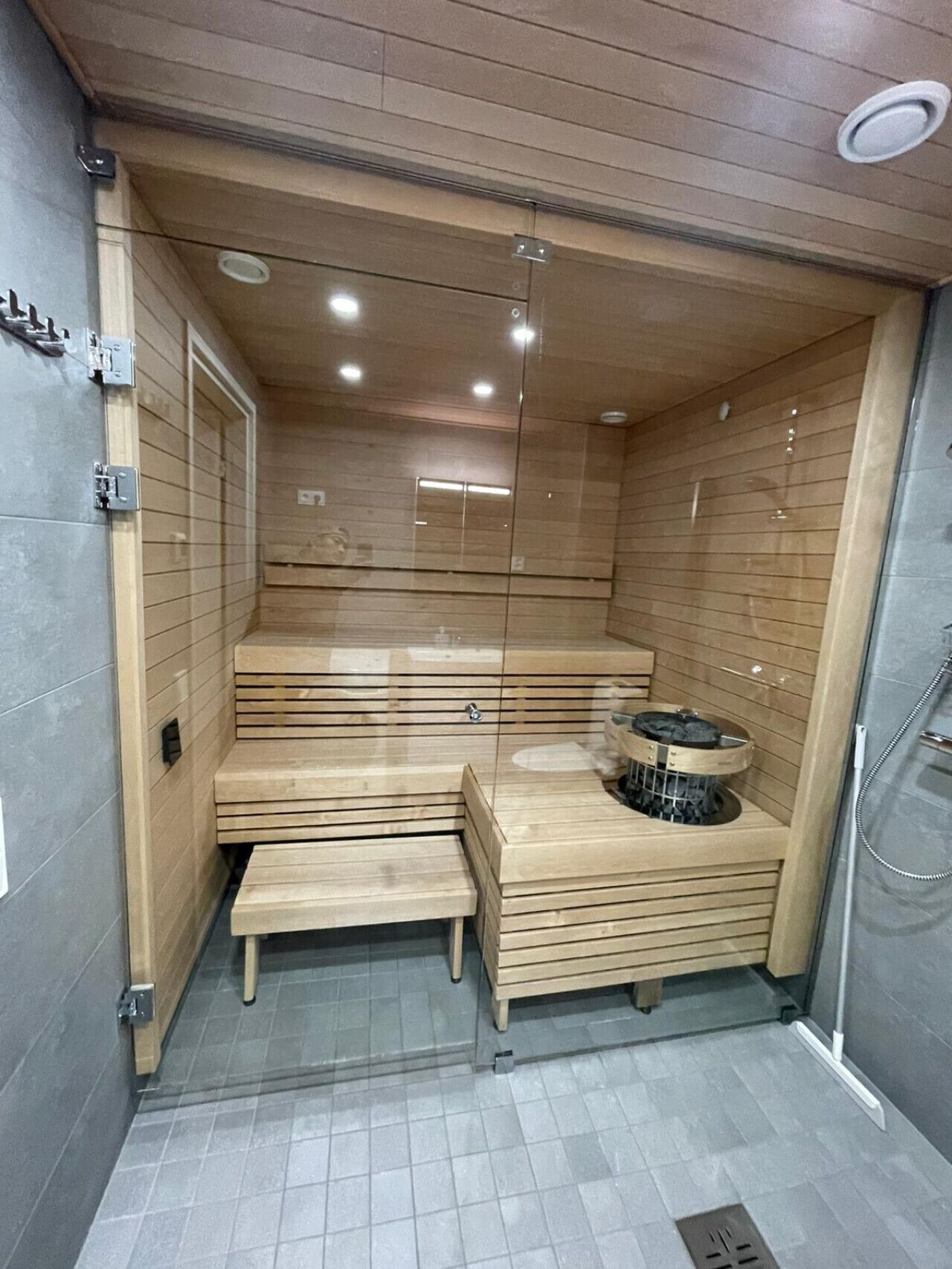 Un sauna con bancos de madera, un calentador central y una puerta de cristal.