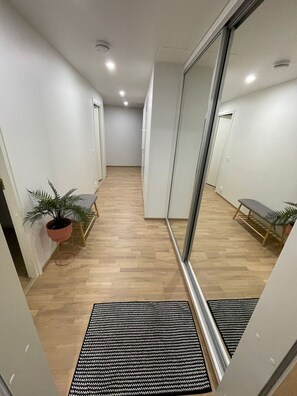 Um corredor com parede espelhada, piso de madeira, planta em vaso, um banco e tapete de entrada.