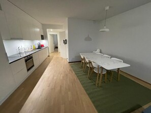 Cozinha moderna com armários brancos e piso de madeira, que dá acesso a uma sala de jantar com mesa e cadeiras brancas.