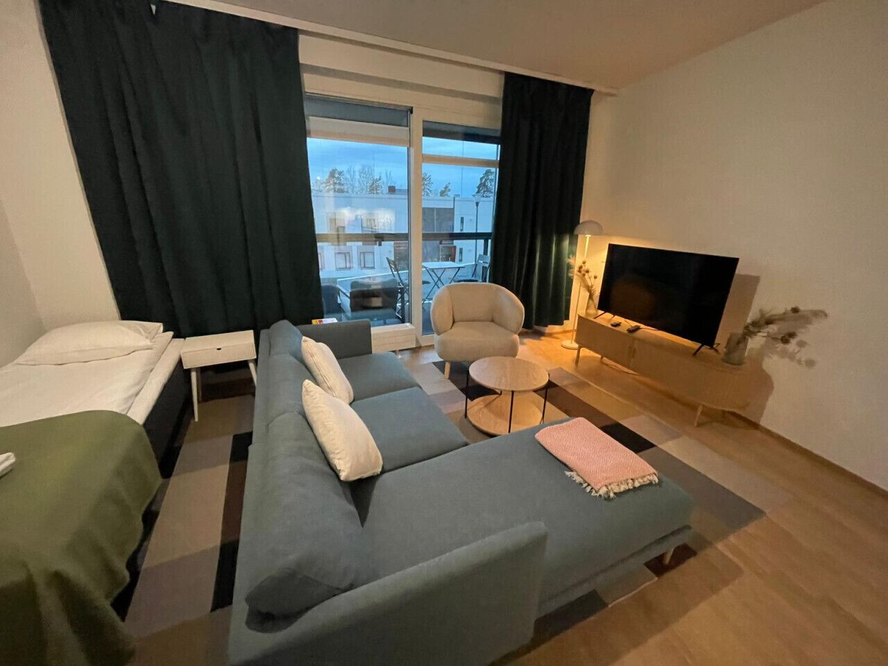 Habitación de hotel moderna con sofá, cama, televisor y balcón con vistas a edificios.