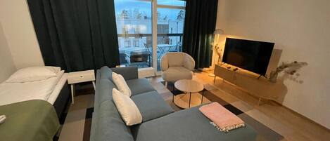 Habitación de hotel moderna con sofá, cama, televisor y balcón con vistas a edificios.