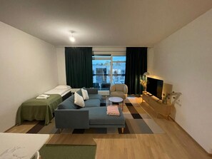 Ein Hotelzimmer mit Sofa, Sessel, kleinem Tisch, Fernseher und einem Fenster mit Vorhängen.