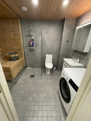 Ein kleines Badezimmer mit Dusche, Toilette, Waschbecken und einer Waschmaschine.