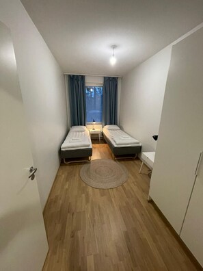 Ein kleines Zimmer mit zwei Einzelbetten, einem runden Teppich, einem kleinen Tisch und einem Fenster mit Vorhängen.