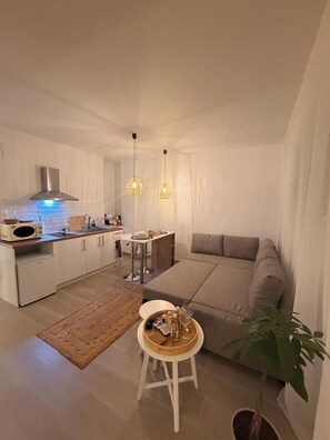 Ett modernt vardagsrum med ett litet kök, en matplats och en sittgrupp med en soffa och ett litet bord.