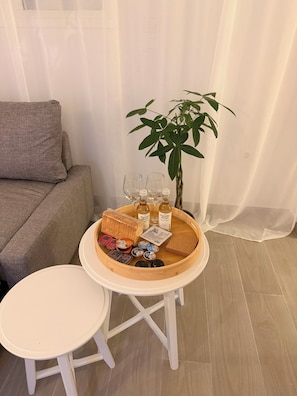 A round wooden tray with food items and drinks on a white table, a grey sofa, and a potted plant in a room with light-colored flooring. - Apartment in Thiseio, just a stone's throw from the Acropolis (Athina)
