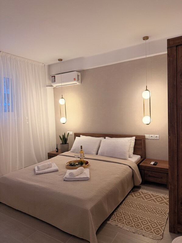 A neatly made bed with a beige blanket, a bedside table with a bottle and glasses, and a patterned rug. - Apartment in Thiseio, just a stone's throw from the Acropolis (Athina)