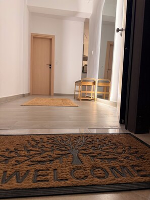 A hallway with a wooden door, two wooden chairs, a welcome mat, and a doormat with a tree design. - Apartment in Thiseio, just a stone's throw from the Acropolis (Athina)