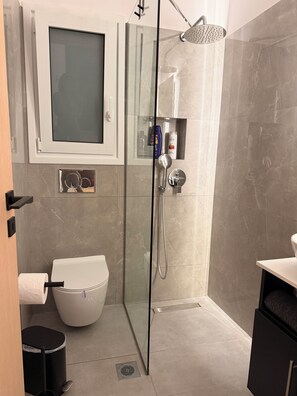 A modern bathroom with a glass-enclosed shower, a toilet, and a vanity with a mirror. - Apartment in Thiseio, just a stone's throw from the Acropolis (Athina)