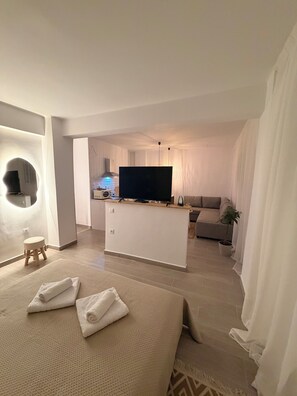 A modern hotel room with a large bed, a flat-screen TV, a sofa, and a small table with a lamp. - Apartment in Thiseio, just a stone's throw from the Acropolis (Athina)