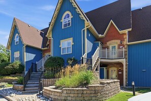 A two-story residential building with a blue exterior, a brick section, and a small front porch with steps leading to the entrance. - Charming Snowbridge Condo with Summer Pool (The Blue Mountains)