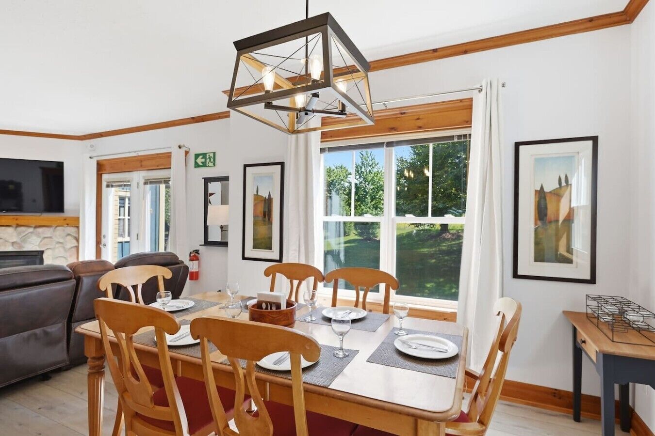 A dining area with a wooden table set for four, surrounded by chairs, a modern pendant light, and framed artwork on the walls.