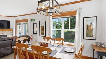 A dining area with a wooden table set for four, surrounded by chairs, a modern pendant light, and framed artwork on the walls.