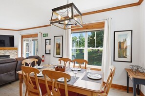 A dining area with a wooden table set for four, surrounded by chairs, a modern pendant light, and framed artwork on the walls. - Charming Snowbridge Condo with Summer Pool (The Blue Mountains)