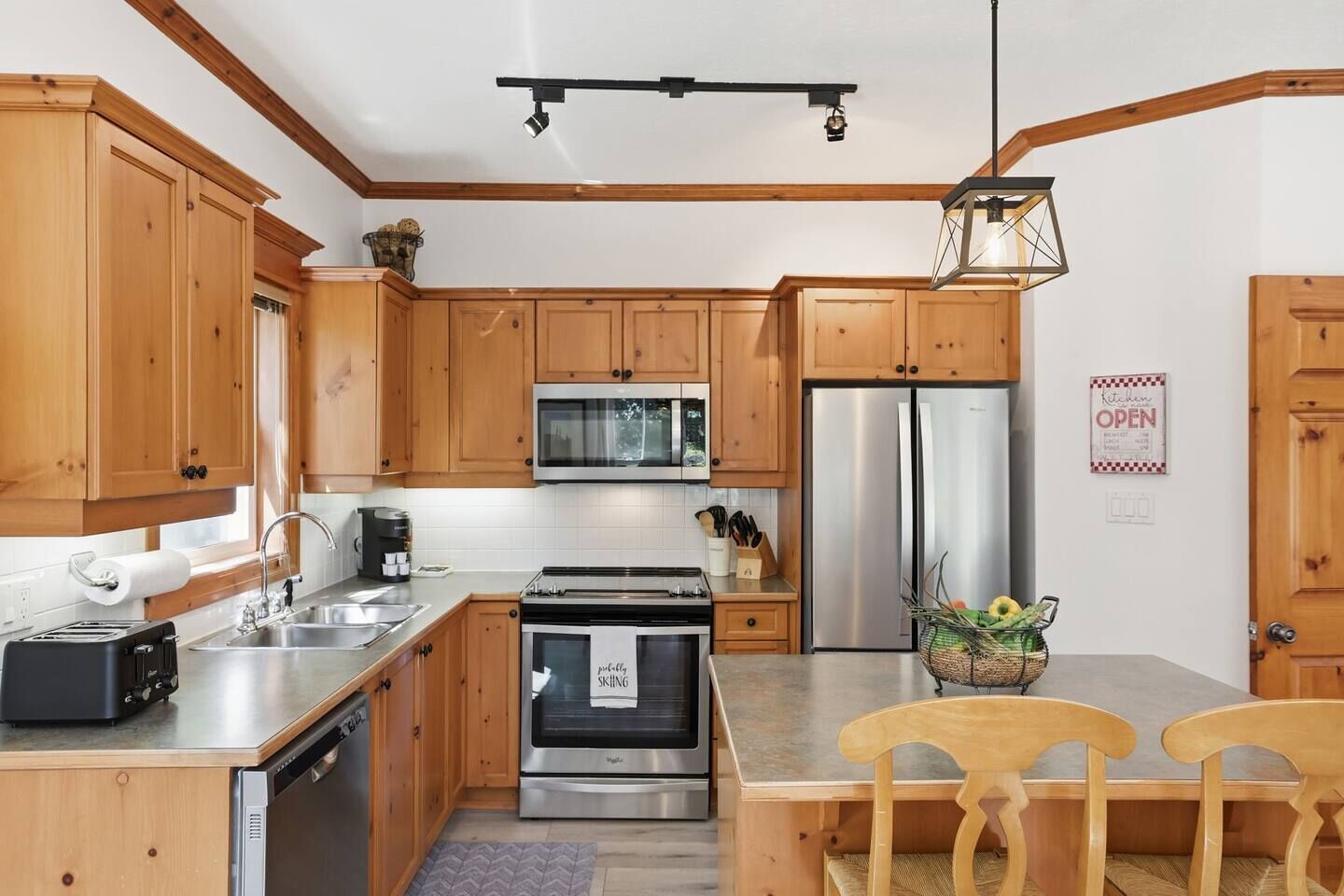 A modern kitchen with wooden cabinets, stainless steel appliances, and a dining area with two wooden chairs.