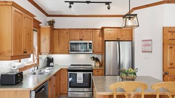 A modern kitchen with wooden cabinets, stainless steel appliances, and a dining area with two wooden chairs.