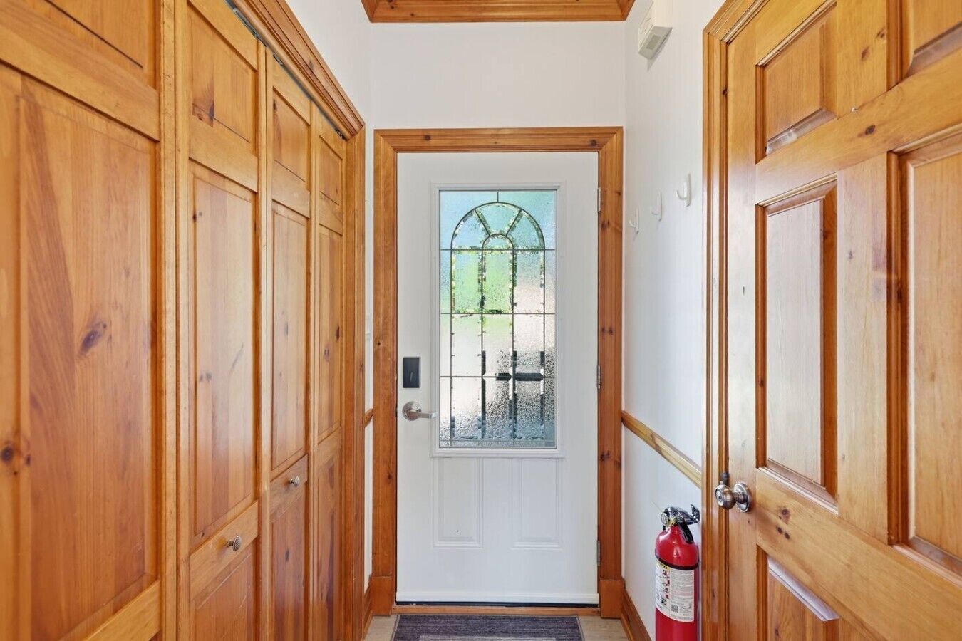 A wooden door with a glass window, a fire extinguisher, and a doormat.