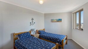 A bedroom with two single beds, a wall-mounted light fixture, a painting, and a window with a view. - Eagle Wings - Stunning Ocean Views - Unit 16 (The Entrance)