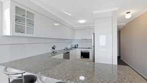 A modern kitchen with white cabinetry, a granite countertop, and stainless steel appliances. - Eagle Wings - Stunning Ocean Views - Unit 16 (The Entrance)