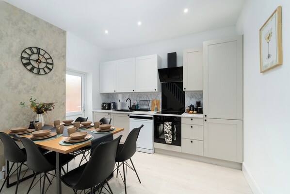 Una cocina moderna con armarios blancos, una campana extractora negra y un comedor con mesa de madera y sillas negras.