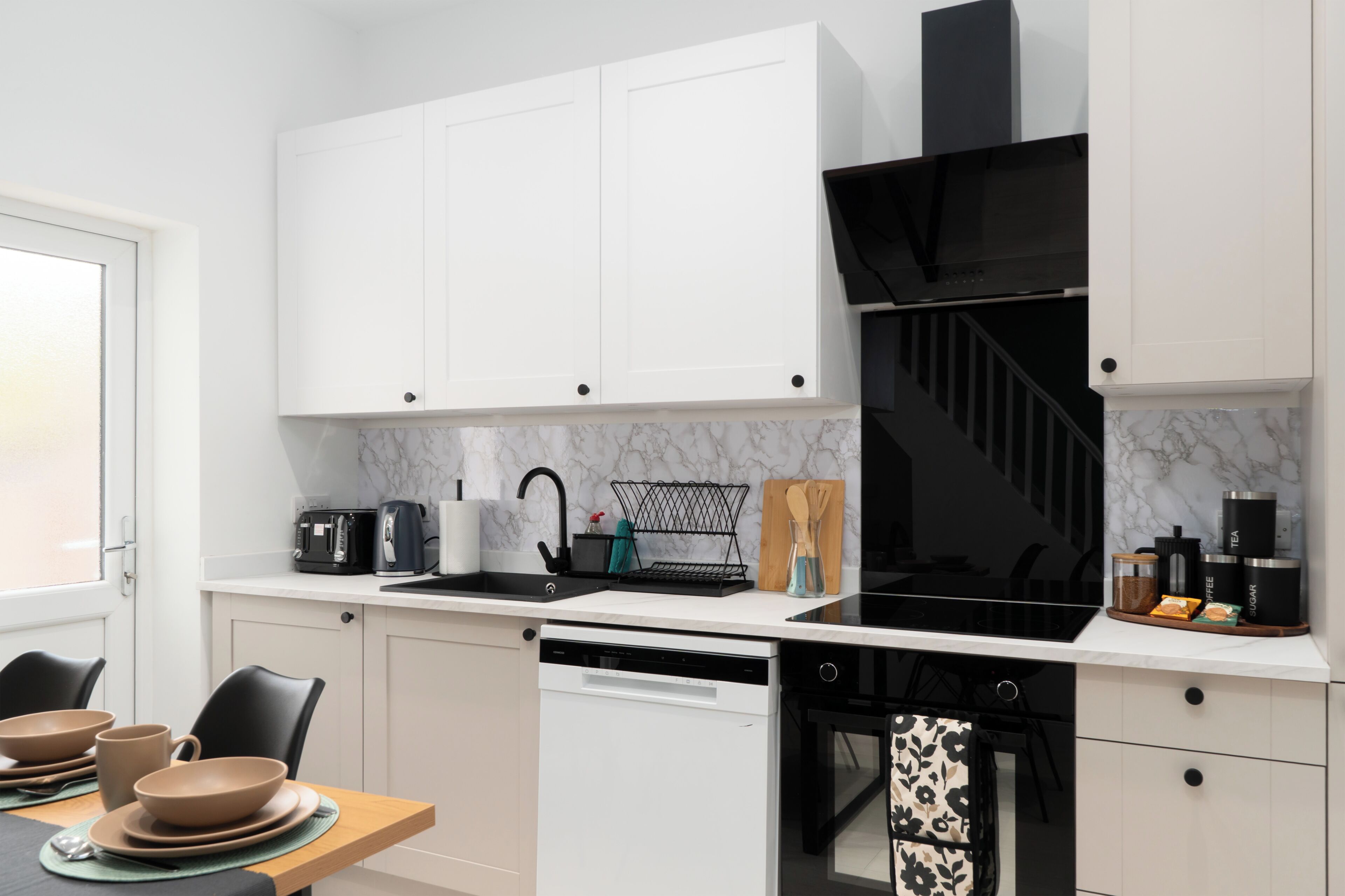 A modern kitchen with white cabinets, a black range hood, and a dining area with a table set for two.