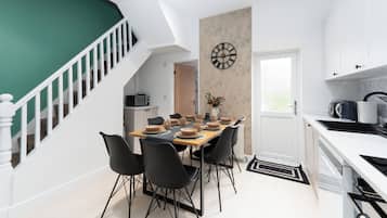 Cozinha moderna com armários brancos, bancada preta e área de jantar com mesa de madeira e cadeiras pretas.