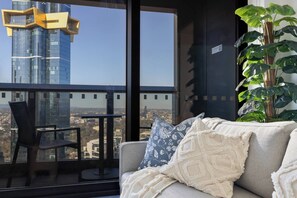 Ein Balkon mit Blick auf eine Stadtlandschaft, eine Couch mit gemusterten Kissen und ein Blumentopf.