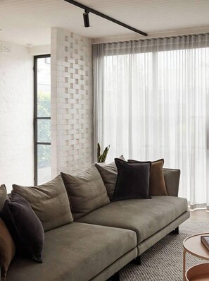 Uma sala de estar moderna com um sofá seccional, uma mesa redonda pequena e uma janela grande com cortinas finas.