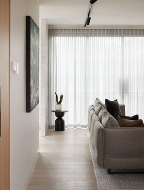 A modern living room with a sofa, a side table with a plant, and a large window with sheer curtains. - The Obscura Stylist Retreat near Cultural Hotspots (Richmond)