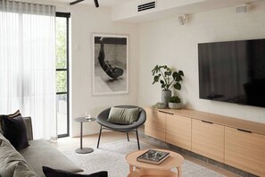 Uma sala de estar moderna com sofá, poltrona, mesa pequena, televisão e planta em vaso.