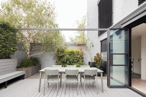 A modern outdoor patio with a dining table and chairs, surrounded by greenery and a white fence. - The Obscura Stylist Retreat near Cultural Hotspots (Richmond)