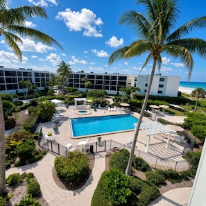 Ein Poolbereich eines Resorts mit klarem, blauem Pool, umgeben von Palmen und einem weißen Gebäude im Hintergrund.