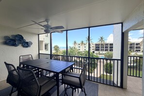 A balcony with a table and chairs, a ceiling fan, and a view of a beach and buildings. - 🐬🐬🐬Beautiful BeachSide at Sea Oats🐬🐬🐬Steps to the Gulf Beach⛱️Sleeps 6🏝️ (Boca Grande)