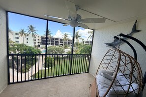 Ein Balkon mit Blick auf einen Pool und Palmen, einem Deckenventilator und einem Hängesessel.