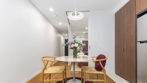 Uma sala de jantar moderna com uma mesa redonda, duas cadeiras, um vaso de flores e uma luminária pendente.