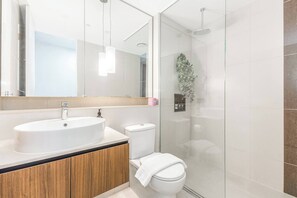 Un baño moderno con un espejo grande, un lavabo, un inodoro y una ducha con mampara de vidrio.