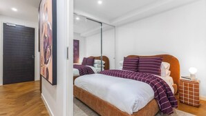 Une chambre à coucher avec un lit, une table de chevet, un miroir et une porte.