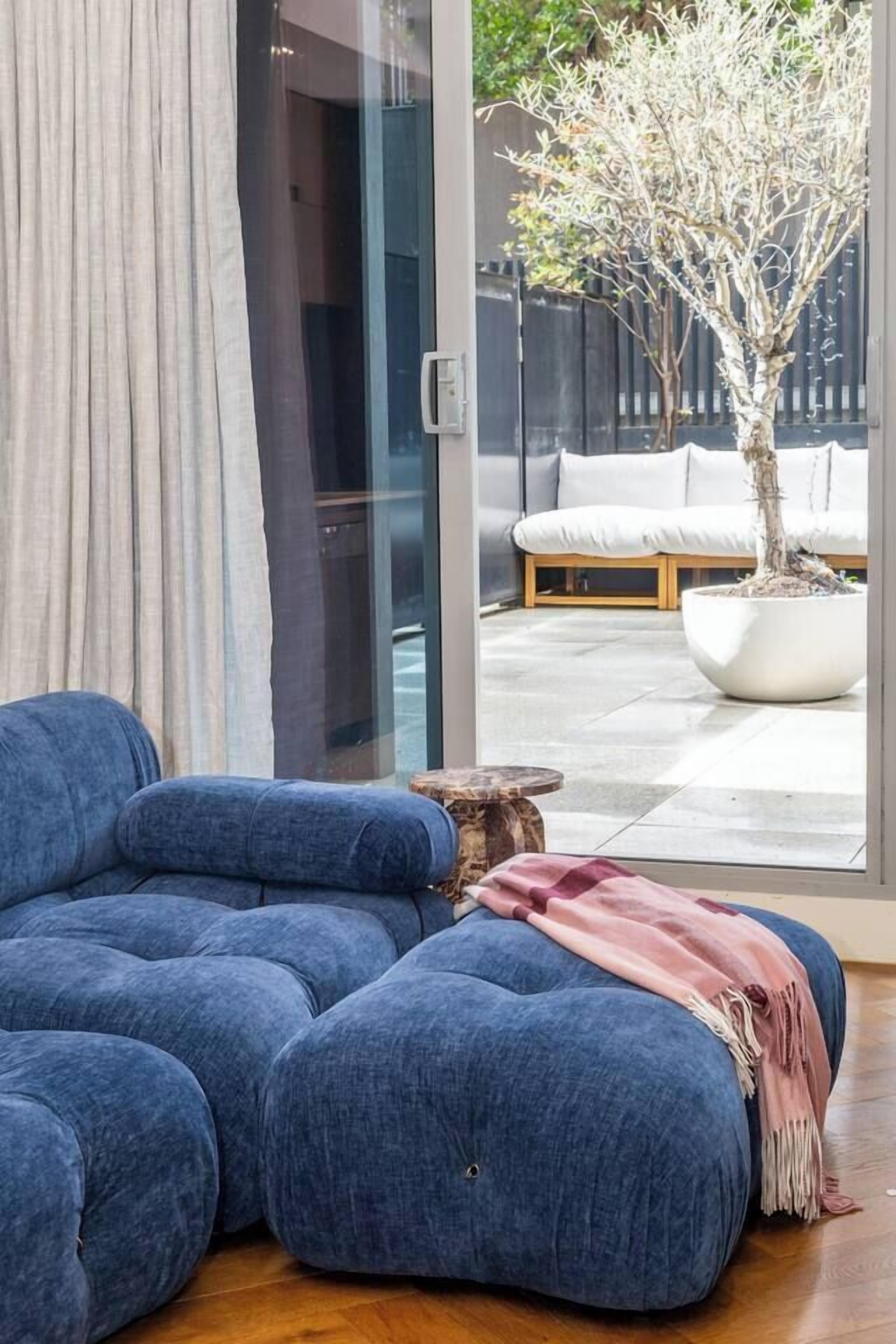 A room with a blue sofa, a wooden stool, and a potted tree.