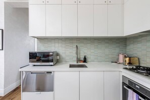 Une cuisine moderne avec des meubles blancs, un lave-vaisselle encastré, une hotte en acier inoxydable et un pare-feu en carrelage.