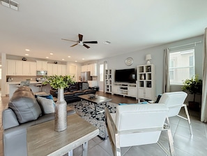 A modern living room with a sofa, coffee table, and TV. There is a kitchen area with cabinets and a refrigerator. - Solara Resort Villa-9BR | Pool & Spa | Near Disney (Kissimmee)