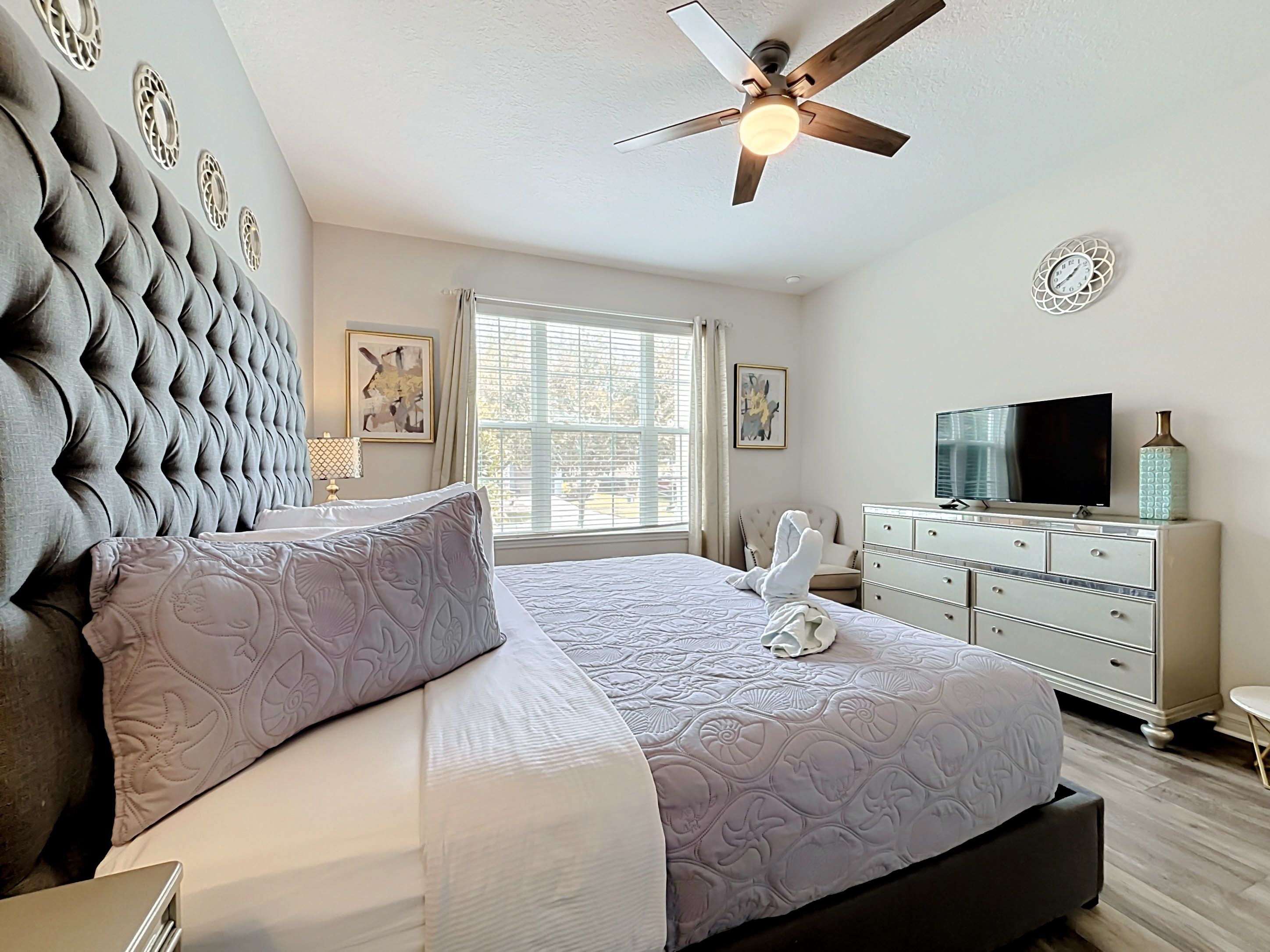 A neatly arranged bedroom with a large bed, a ceiling fan, a television, and a dresser.