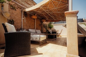 Zona d'estar a l'aire lliure amb llums de sol, moble de vimet, estructura de llit metàl·lica i teulada de palla.