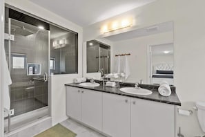 Une salle de bain moderne dotée d’une douche à parois de verre, de deux vasques et d’un grand miroir.