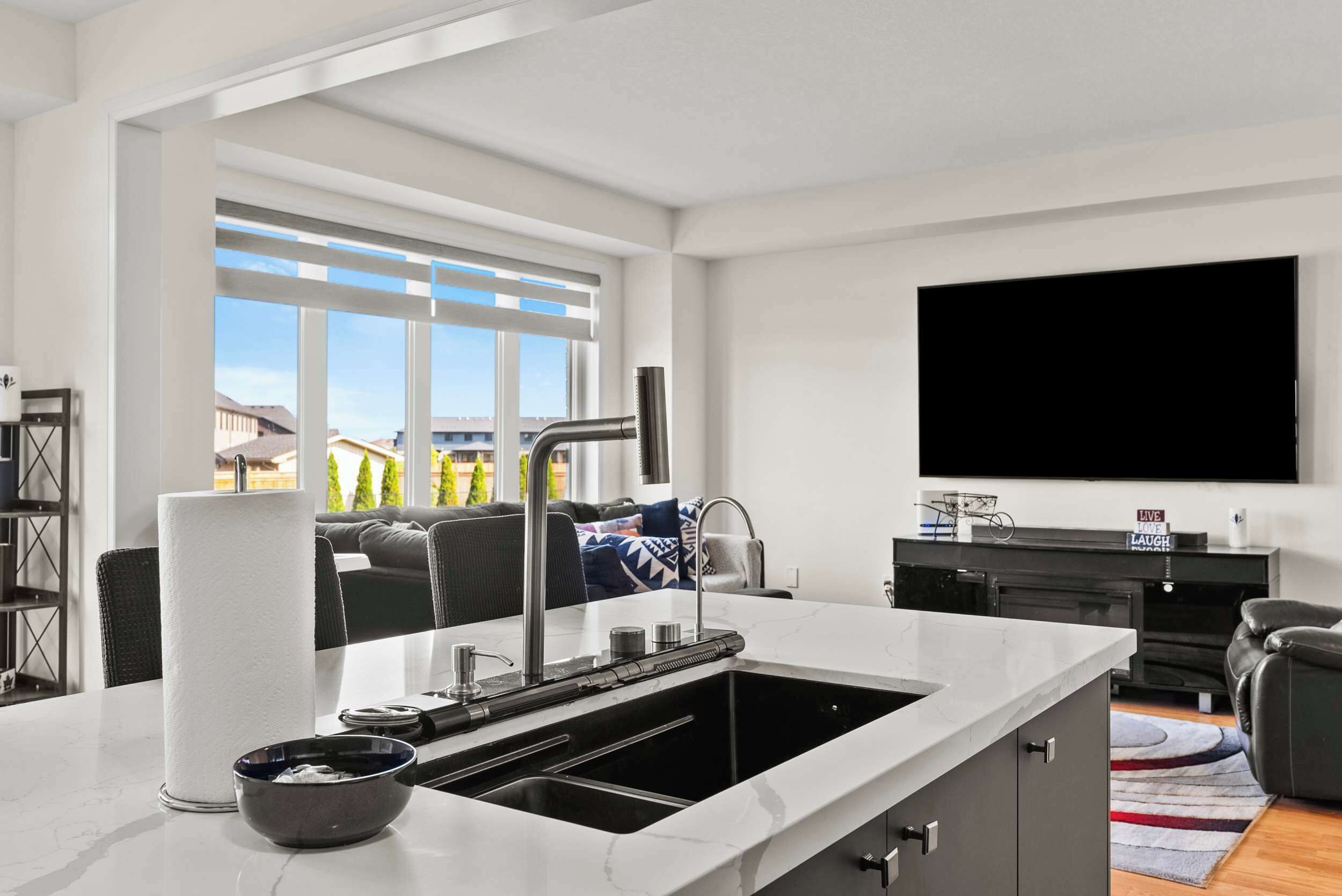 Een moderne keuken met een groot eiland, een inbouwgootsteen en een raam met uitzicht op een woonwijk.
