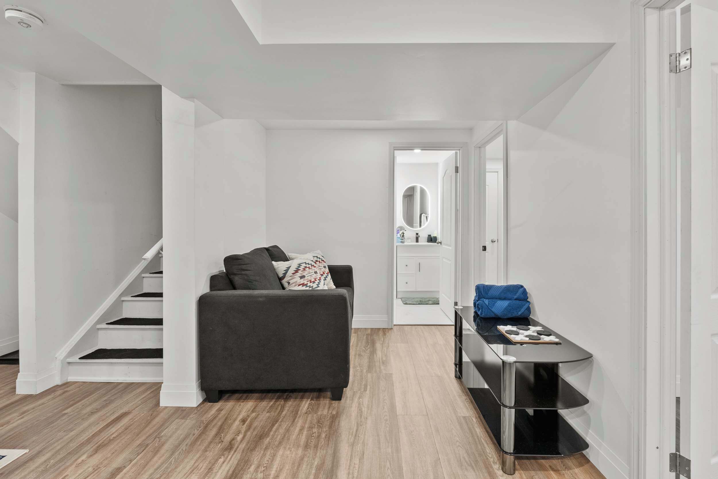 Un salon moderne avec un canapé gris, une petite table et un escalier menant à une autre pièce.