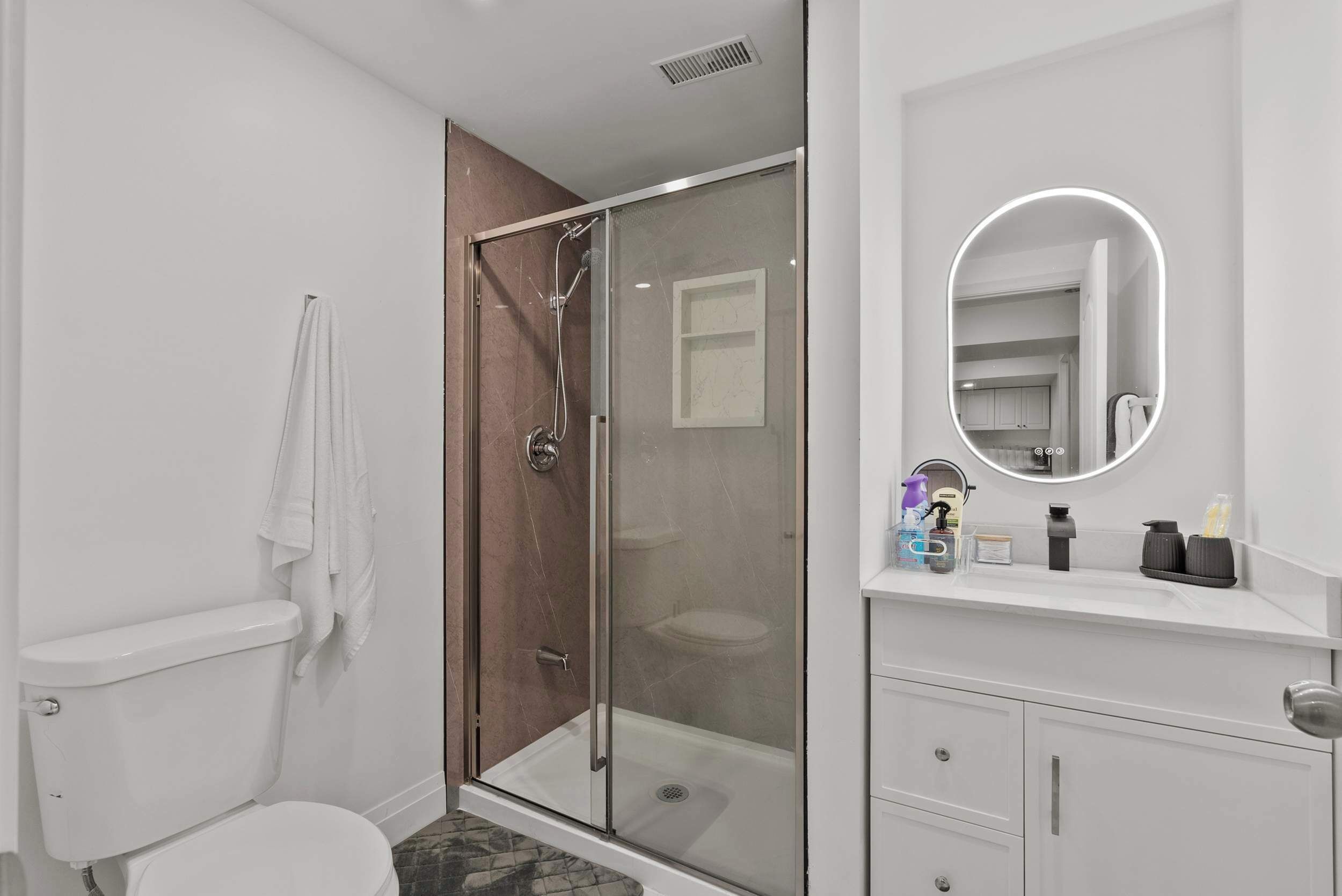 A modern bathroom with a glass-enclosed shower, a white toilet, and a vanity with a mirror.