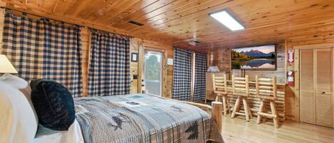 Un dormitorio de cabaña de madera con una cama, cortinas a cuadros, un televisor montado y un extintor.